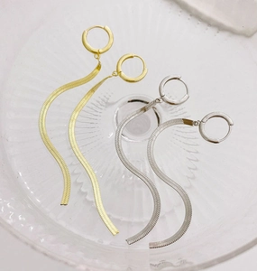 Detail of wavy gold and silver snake chain drop earrings on a glass tray