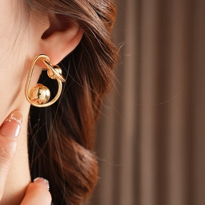 Close-up of a gold geometric twisted ball stud earring worn by a model in detail view