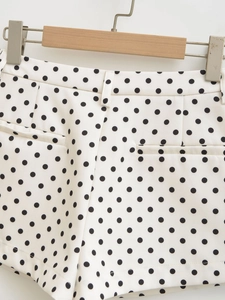 Detail of white polka dot shorts featuring waist design and side pockets on a hanger