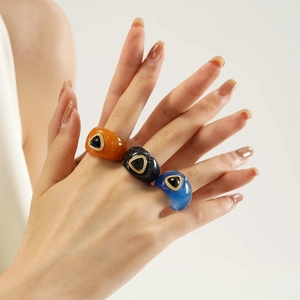 Close-up of three colorful resin rings with golden settings and black stone inlays