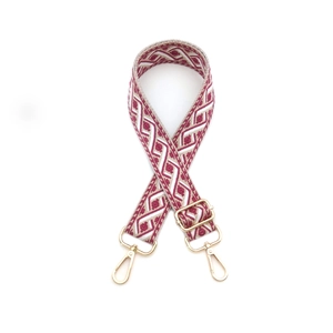 Détail d'une bandoulière tissée rouge et blanc avec mousquetons en métal doré et boucle