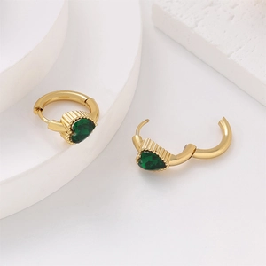 Detail view of gold hoop earrings with green heart-shaped zircons on white marble