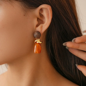Close-up of model wearing resin geometric earrings with gold knot and orange pendant