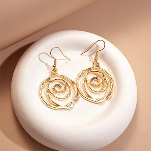 Macro shot of gold hollow spiral rose dangle earrings on a textured white tray