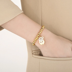 Detailed view of an 18K gold plated beaded bracelet with a cute pig charm on a model's wrist