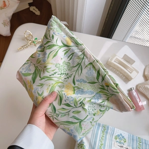 Hand holding a floral cotton makeup bag with green leaves and yellow flowers detail