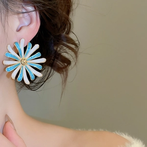 Primo piano di orecchini a margherita blu e bianchi con pistillo dorato sul modello
