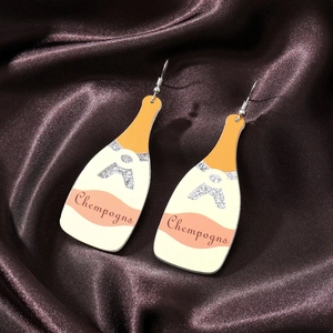 Close-up of champagne bottle earrings with pink labels and silver glitter on brown silk
