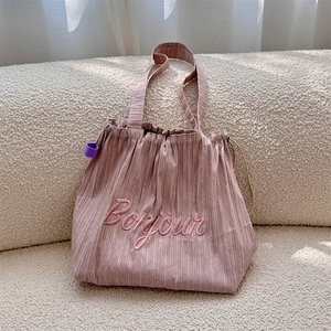 Detail of pink striped canvas tote bag with Bonjour embroidery on a soft tweed sofa