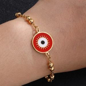 Golden beaded bracelet with evil eye enamel charm worn on model with black background