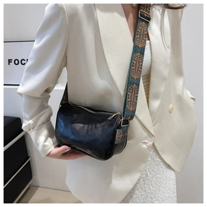 Black barrel crossbody bag featuring a wide ethnic style woven strap on white blazer