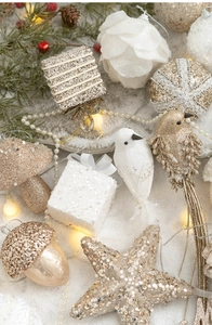 Close-up of assorted white and gold Christmas ornaments on snow background with warm lights