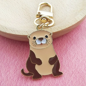 Porte-clés loutre en émail marron avec fermoir doré sur fond en feutre rose et bois