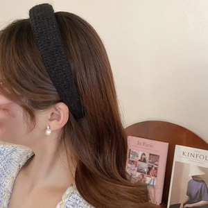 Close-up of black woven headband with subtle shimmer and a classic pearl stud earring
