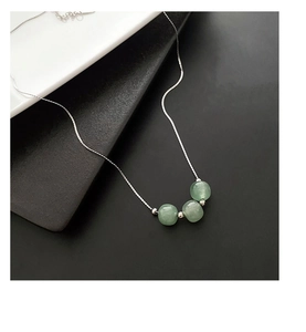 Detail of silver chain necklace featuring three green jade beads on a minimalist stand