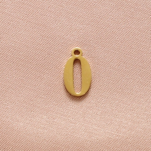 Detailed view of gold number 0 pendant in polished stainless steel on soft pink fabric