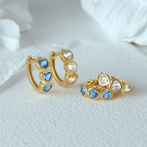 Detail of gold huggie earrings featuring blue and white heart-shaped zircon stones