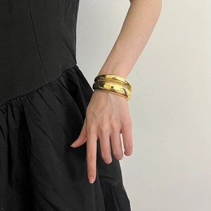 Minimalist double-layered gold metallic bangle with a glossy finish on a model's wrist