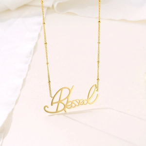 Collier doré avec pendentif Blessed en écriture cursive sur un fond blanc épuré et chic