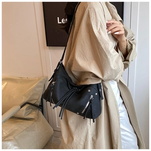 Dettaglio della borsa in pelle nera opaca con frange e zip d'argento su un cappotto beige