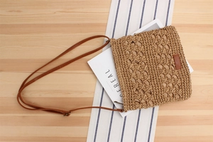 Detail of hand-woven straw crossbody bag with brown leather strap on a rustic table