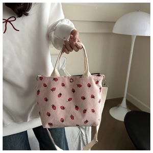 Detailed view of pink corduroy bucket bag with red strawberry pattern and shoulder strap
