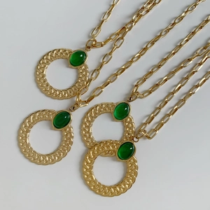 Detail of four gold twist rings with green oval stones on paperclip link chains
