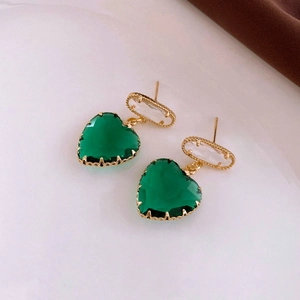 Detail shot of heart-shaped emerald green earrings with golden wavy metal base