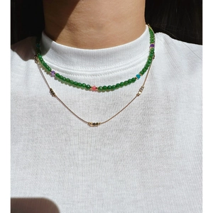 Double-layered gold chain necklace with faceted green stone beads on a model