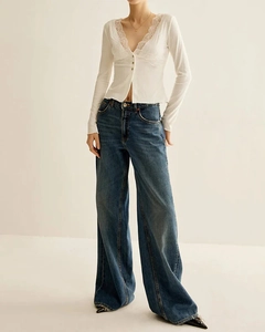 Detail of V-neck white knit top with lace trim and high-waisted wide-leg blue jeans