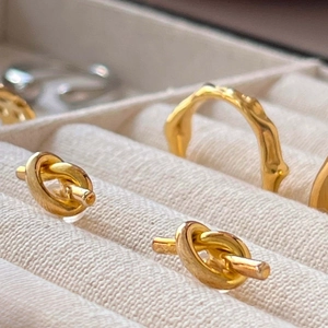 Minimalist gold knot stud earrings and irregular textured ring on a velvet jewelry display