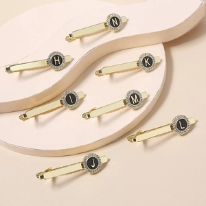 Detailed macro view of gold-tone necktie clips with crystal alphabet letters H to N