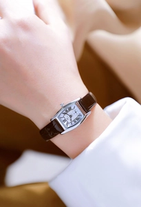 Detail of silver rectangular quartz watch with brown leather strap and Roman numerals on wrist