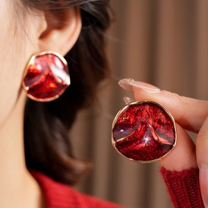 Detail view of light luxury gold round earrings with red textured enamel on model
