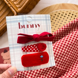 Close-up of red fabric bow hair clips and embroidered velvet barrette set on card