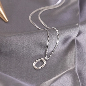Detailed view of silver minimalist necklace with irregular oval pendant on grey silk fabric