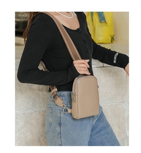Detail of beige crossbody chest bag featuring double zippers and a striped fabric strap