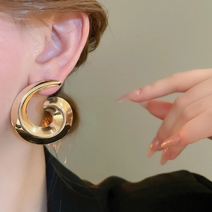 Close-up of a large golden spiral metal earring on a model's ear with high gloss finish