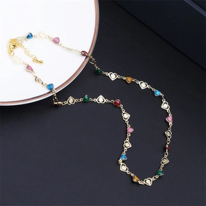 Close-up of golden necklace with colorful glitter hearts and hollow charms on a white plate