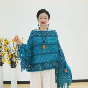 Detail of teal knitted poncho with geometric patterns and fringe edges on a model