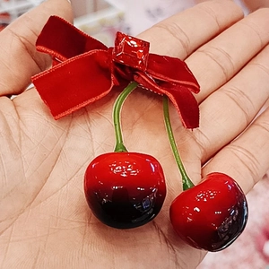 Détail de la barrette à nœud en velours rouge avec breloques cerise et gemme carrée