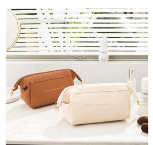 Dettaglio di trousse in pelle PU color caramello e beige con cerniera dorata su marmo