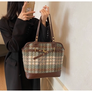 Detail of plaid fabric and brown leather tote bag with metal buckle on a fashion model