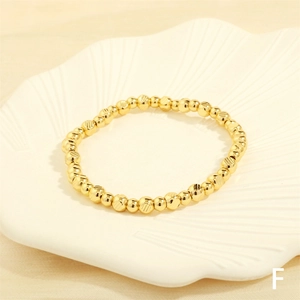 Detailed view of irregular gold beaded stretch bracelet on a white textured shell tray