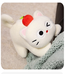 Detailed view of white plush cat toy with apple hat on a soft green knit blanket