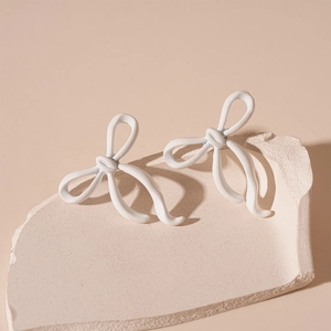 Detailed view of white painted bow-knot stud earrings on a minimalist decorative stone