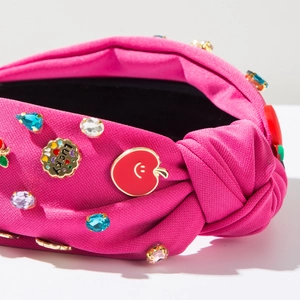 Macro view of magenta fabric headband featuring rhinestones and a red apple enamel charm