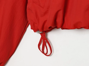 Detail of red nylon jacket hem featuring adjustable drawstring and metal spring buckle