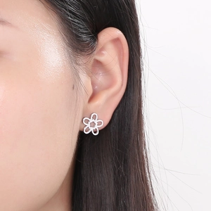 Close-up of silver hollow five-petal flower earring worn on ear showing realistic size