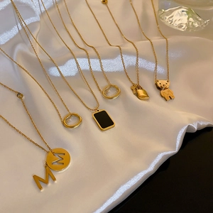 Dettaglio dei ciondoli a forma di orso d'oro e lettera M su collana in acciaio al titanio